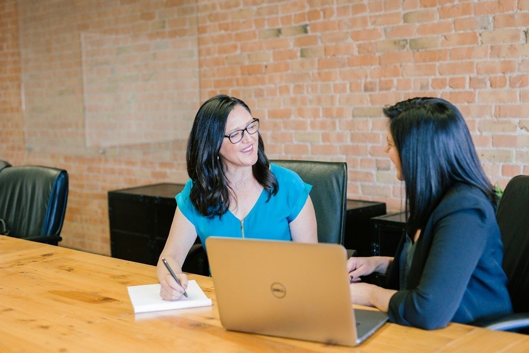 Zwei Frauen besprechen sich an einem Tisch mit Laptop und Notizen