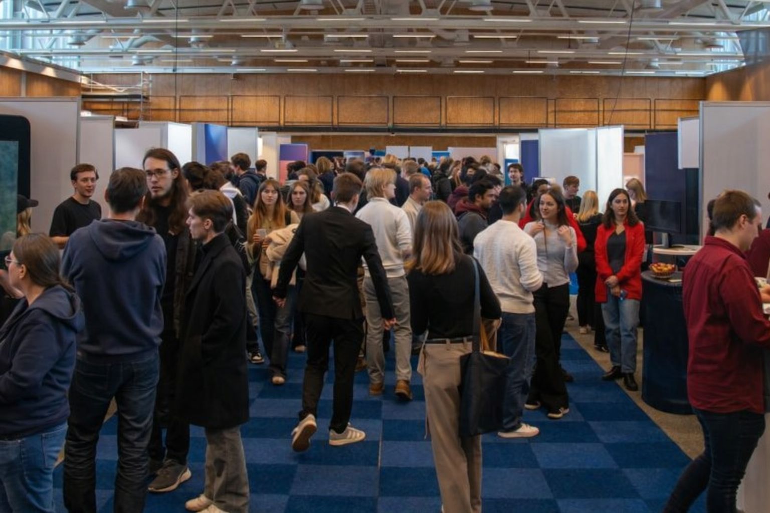 Menschenmenge auf einer Bildungsmesse mit Ständen und Studenten in Gesprächen.